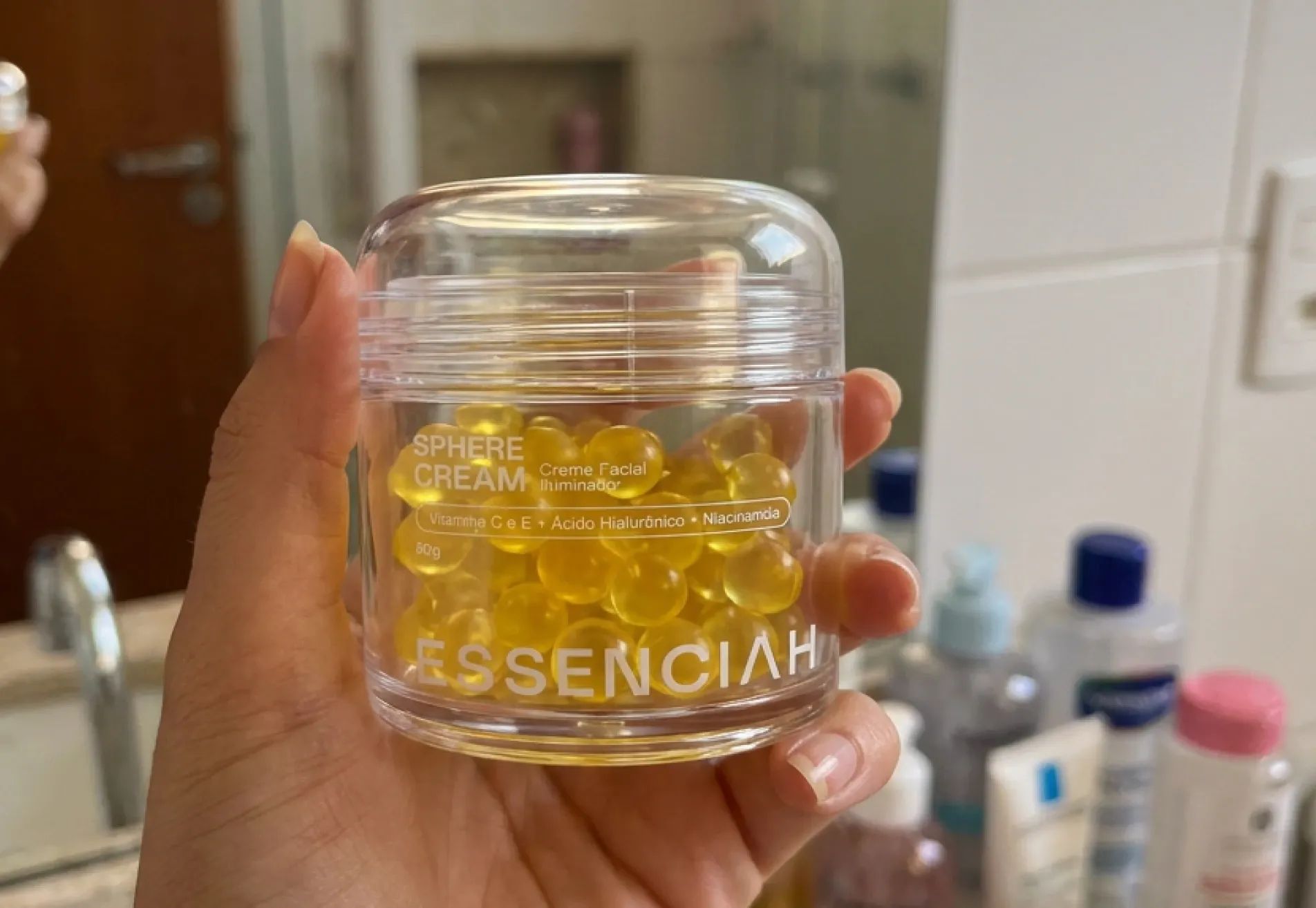 Mão segurando o pote de Sphere Cream no banheiro